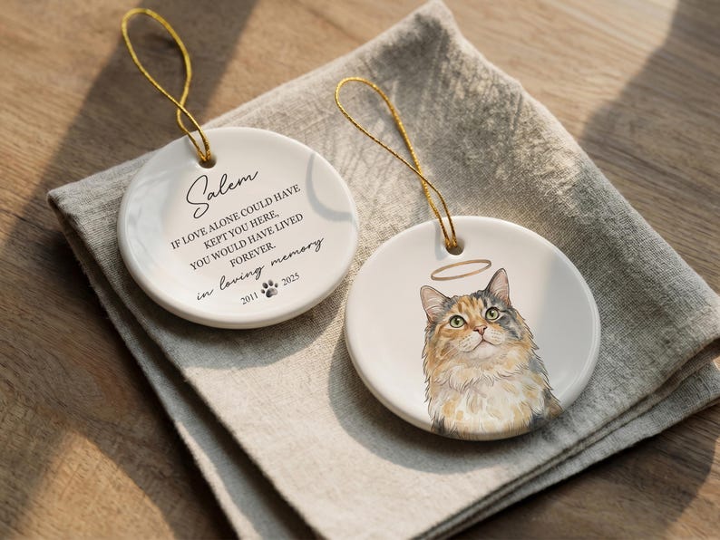 May include: Two round white ceramic ornaments with gold hanging strings. One features the text Salem, If love alone could have kept you here, you would have lived forever, in loving memory, 2011 paw print 2025. The other shows a calico cat with a halo.