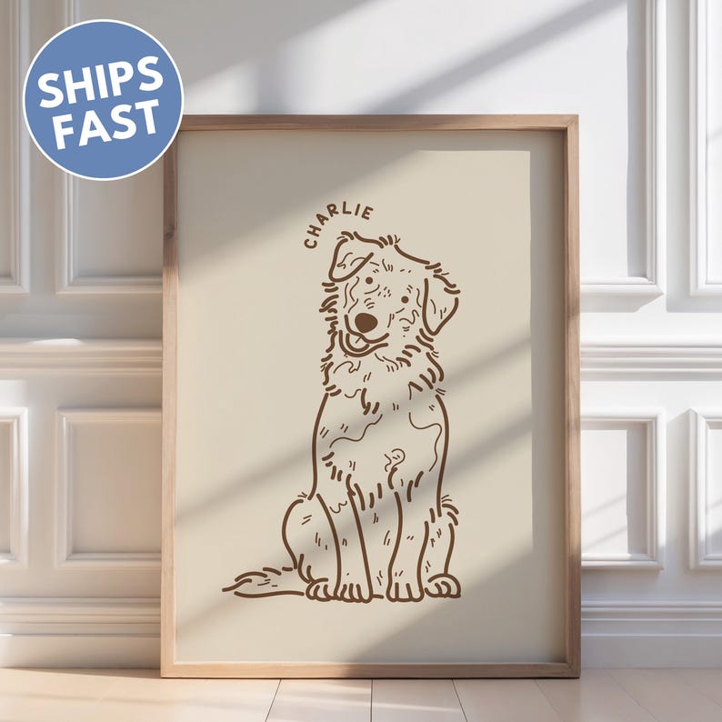 May include: A framed print featuring a brown line drawing of a dog named Charlie. The dog is sitting with its tongue out. The background is a light beige color. The frame is a light brown color. A blue circle with the words "SHIPS FAST" is in the upper left corner.
