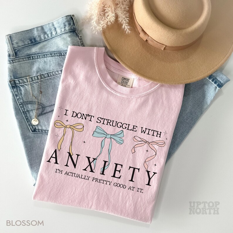 May include: Pink t-shirt with the text "I don't struggle with anxiety. I'm actually pretty good at it." and three colorful bows.