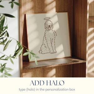 May include: A framed print featuring a doodle dog illustration with a halo. The dog is drawn in a simple, line art style with the name "KRATOS" on the side. The print is displayed on a wooden shelf, with the text "ADD HALO" below.