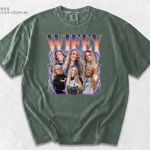 May include: Moss green t-shirt with a graphic of the word "WIFEY" in a retro font, with a group of women's faces in a purple and white lightning bolt design. The shirt has a crew neck and short sleeves.