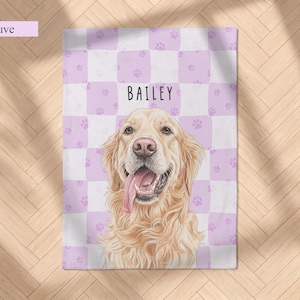 May include: A rectangular blanket featuring a mauve and white checkered pattern with small paw prints. Centered is a detailed illustration of a golden retriever with its tongue out, and the name BAILEY printed in black above the dog.