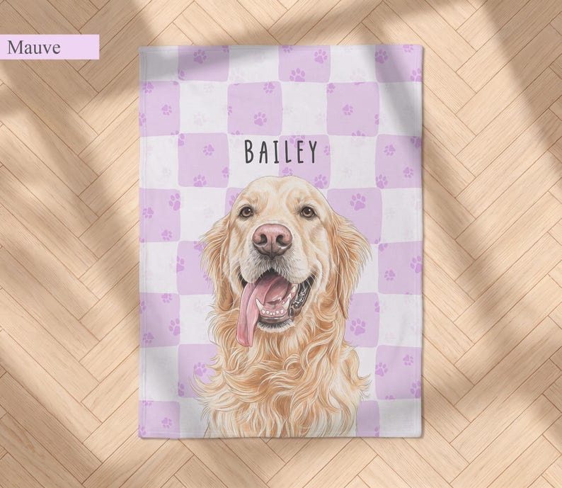 May include: A rectangular blanket featuring a mauve and white checkered pattern with small paw prints. Centered is a detailed illustration of a golden retriever with its tongue out, and the name BAILEY printed in black above the dog.