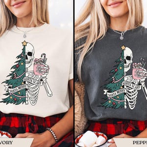 May include: Ivory and pepper-colored t-shirts with a festive, yet spooky design. The graphic features a half-skeleton, half-Christmas tree with the text "Sorta Merry Sorta Scary". The skeleton holds a mug with candy canes.