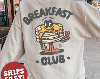 May include: A light gray sweatshirt with a cartoon pancake character wearing a peace sign and the text "Breakfast Club."