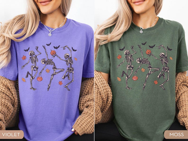 K&ouml;nnte beinhalten: Zwei kurz&auml;rmelige T-Shirts mit Rundhalsausschnitt, eines in Violett und eines in Moosgr&uuml;n, jeweils mit einem Grafikdruck von drei tanzenden Skeletten zwischen orangefarbenen Herbstbl&auml;ttern, schwarzen Flederm&auml;usen und kleinen K&uuml;rbiseimern.
