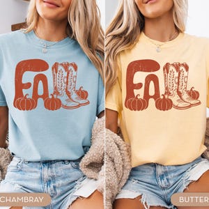 May include: Two short-sleeved t-shirts, one light blue and one yellow, each with a distressed orange graphic. The graphic says "FALL" with pumpkins and cowboy boots. The bottom of the shirts are visible.
