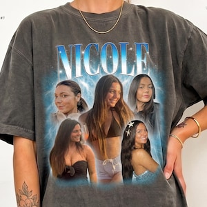 May include: A charcoal gray t-shirt featuring the name NICOLE in large blue letters at the top. Below the name, a collage of five photographs shows the same person in various settings. The text PEPPER DESIGN COLOR #7 and UPTOPNORTH are visible.