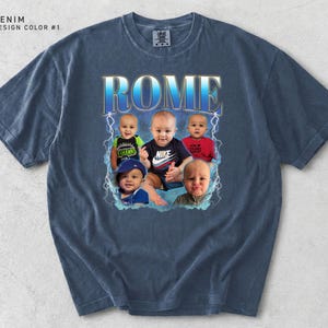 May include: Denim blue t-shirt with a graphic design featuring the word "ROME" in a blue and gold font, with images of five babies. The shirt has a crew neck and short sleeves. The text "DENIM DESIGN COLOR #1" is in the upper left corner.