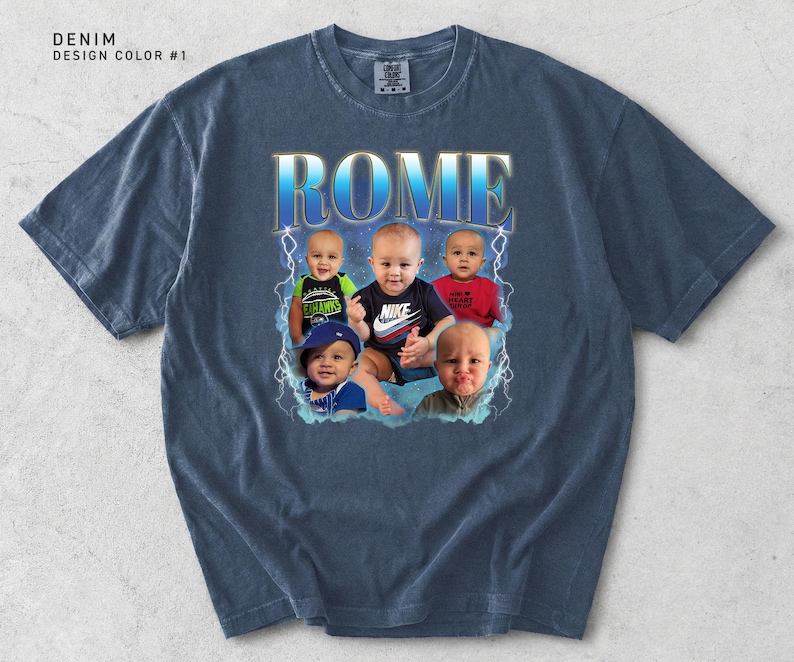 May include: Denim blue t-shirt with a graphic design featuring the word "ROME" in a blue and gold font, with images of five babies. The shirt has a crew neck and short sleeves. The text "DENIM DESIGN COLOR #1" is in the upper left corner.