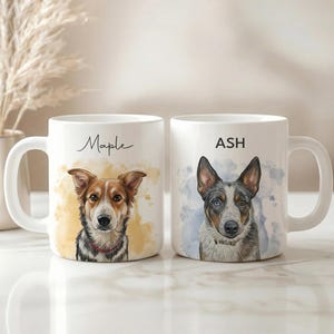 May include: Two white ceramic mugs with dog portraits. One mug has the name "Maple" and a portrait of a brown and white dog. The other mug has the name "ASH" and a portrait of a blue and gray dog. Both mugs have a white handle.