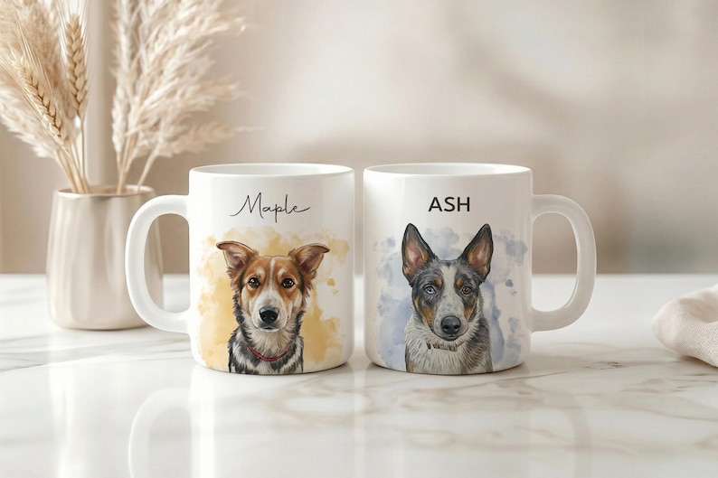 May include: Two white ceramic mugs with dog portraits. One mug has the name "Maple" and a portrait of a brown and white dog. The other mug has the name "ASH" and a portrait of a blue and gray dog. Both mugs have a white handle.