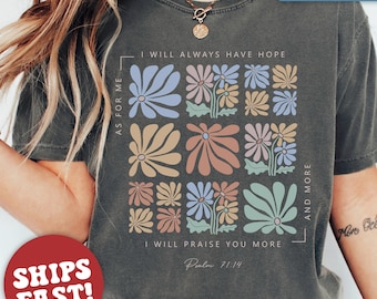 May include: A charcoal grey t-shirt with a floral design and the text "As for me, I will always have hope. I will praise you more. Psalm 71:14. And more."