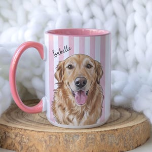 May include: A ceramic mug with a pink handle and interior, featuring a vertical white and pink striped pattern. The front displays a detailed illustration of a golden retriever dog with its tongue out, with the name Isabelle printed above.