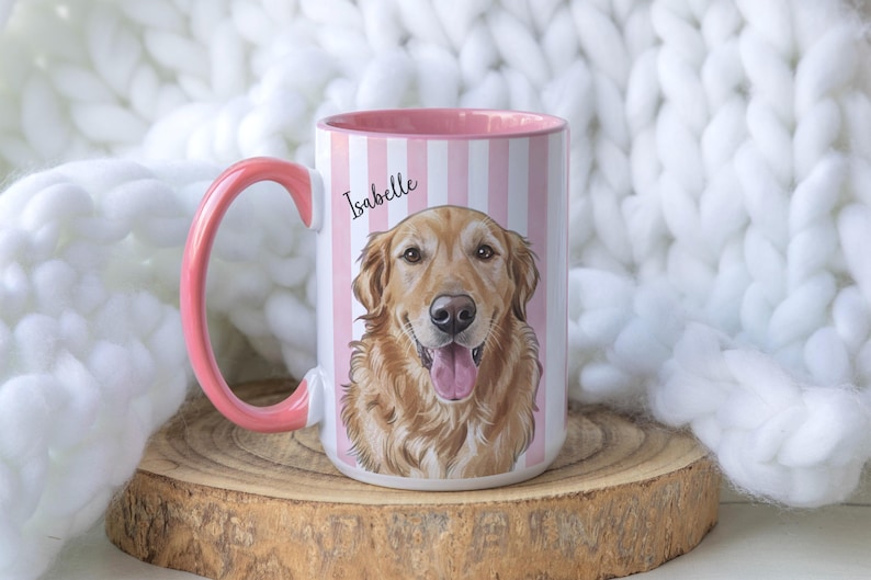 May include: A ceramic mug with a pink handle and interior, featuring a vertical white and pink striped pattern. The front displays a detailed illustration of a golden retriever dog with its tongue out, with the name Isabelle printed above.