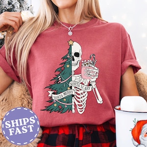 May include: A maroon t-shirt with a graphic featuring a half Christmas tree and a half skeleton holding a mug with candy canes. The text reads "Sorta Merry" and "Sorta Scary".