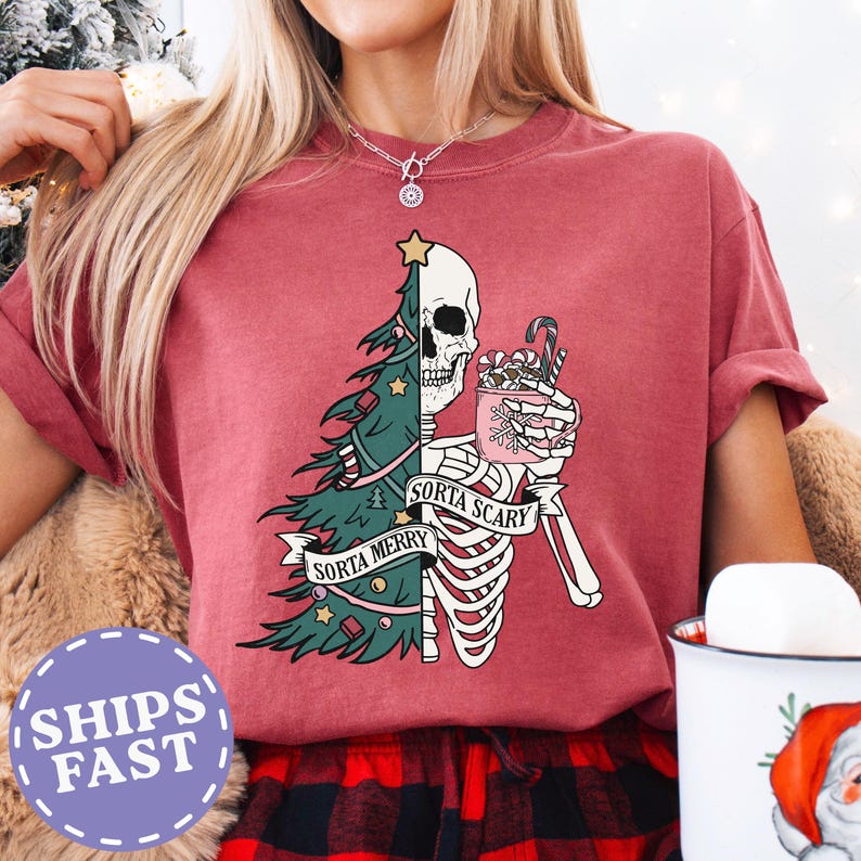 May include: A maroon t-shirt with a graphic featuring a half Christmas tree and a half skeleton holding a mug with candy canes. The text reads "Sorta Merry" and "Sorta Scary".