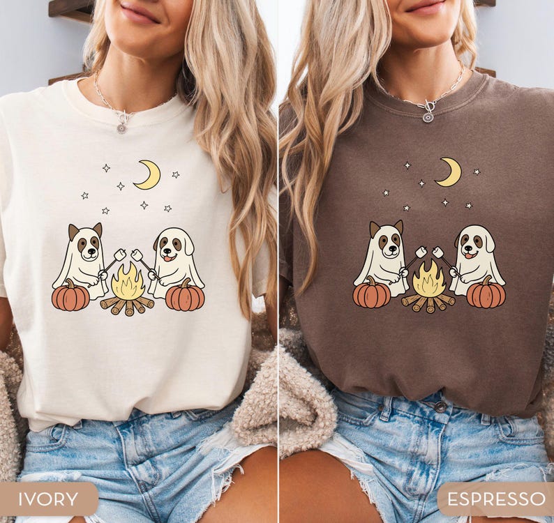 May include: Ivory and espresso-colored t-shirts featuring a graphic of two dogs dressed as ghosts roasting marshmallows over a campfire, with pumpkins, a crescent moon, and stars. The shirts are made of soft material.