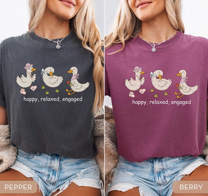 May include: Two t-shirts, one pepper and one berry, each featuring a cartoon design of three ducks. The ducks are wearing hats, bows, and scarves, and are walking on grass. The text "happy, relaxed, engaged" is below the ducks.