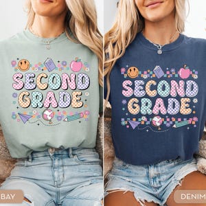 May include: Two t-shirts, one in bay green and the other in denim blue, each featuring the words "SECOND GRADE" in a colorful, retro font. The design includes a smiling face, apple, book, globe, pencil, and paper airplane. The shirts are casual and suitable for students.