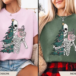 May include: Pink and green t-shirts with a skeleton graphic. The graphic features a skull, Christmas tree, and the text "Sorta Merry Sorta Scary". The skeleton holds a mug with candy canes.