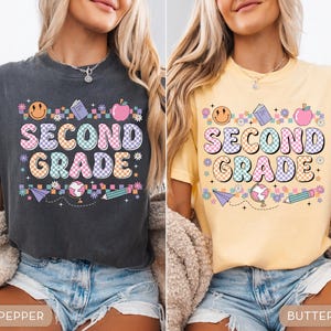 May include: Two t-shirts, one pepper-colored and one butter-colored, each featuring a colorful "SECOND GRADE" graphic. The design includes a smiley face, book, apple, flowers, paper airplane, globe, and pencil. The shirts are a comfortable, casual style.