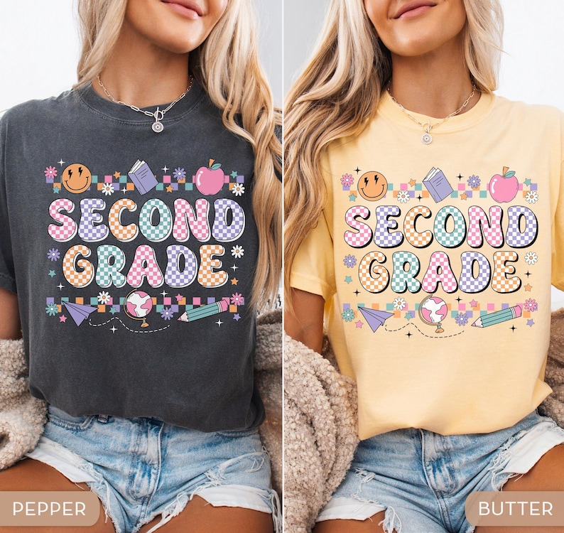 May include: Two t-shirts, one pepper-colored and one butter-colored, each featuring a colorful "SECOND GRADE" graphic. The design includes a smiley face, book, apple, flowers, paper airplane, globe, and pencil. The shirts are a comfortable, casual style.