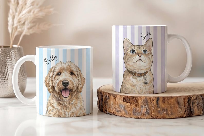 May include: Two white ceramic mugs featuring custom pet illustrations. The left mug displays a golden-colored dog with the name Billy, set against light blue vertical stripes. The right mug shows a tan cat with the name Suki, set against light purple vertical stripes.