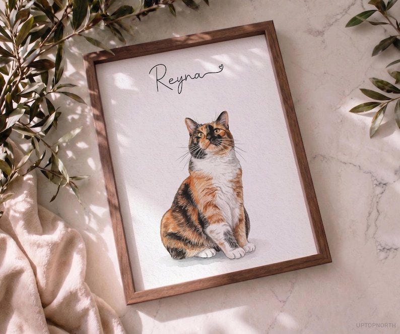 Op de afbeelding: Een ingelijste print met een gedetailleerde illustratie van een zittende lapjeskat. De kat heeft oranje, zwarte en witte vacht. Boven de kat staat de naam Reyna in zwarte cursieve letters met een klein hartje aan het einde.