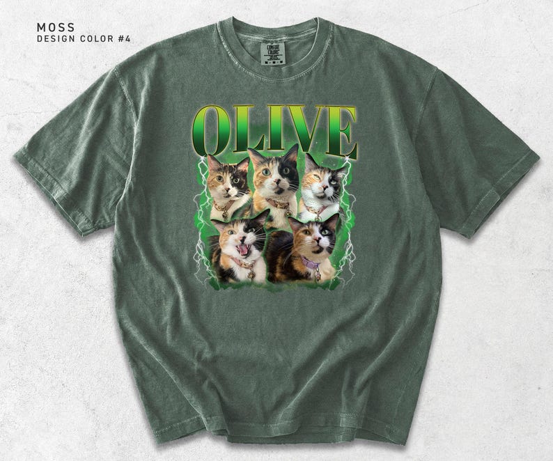 May include: A moss green short-sleeve t-shirt featuring a graphic print of five calico cats. Above the cats, the word OLIVE is printed in a green and yellow gradient font. The design includes white lightning bolt accents surrounding the cats.