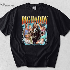 May include: Black t-shirt with a graphic design featuring the text "BIG DADDY" in orange and yellow, with a collage of images. The design includes a retro aesthetic with lightning bolt accents.