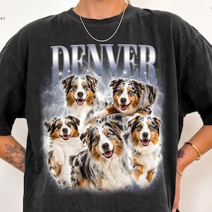 May include: A black short-sleeve t-shirt featuring the word DENVER in large silver metallic-style lettering at the top. Below the text is a graphic collage of five Australian Shepherd dogs with blue merle and brown fur, set against a hazy, glowing background.