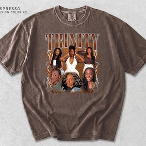 K&ouml;nnte beinhalten: Espressofarbenes T-Shirt mit einem Grafikdesign mit dem Wort "TRINITY" in einer Vintage-Schriftart. Die Grafik enth&auml;lt Bilder von sechs Frauen. Das Shirt hat einen Rundhalsausschnitt und kurze &Auml;rmel. Die Designfarbe ist #9.