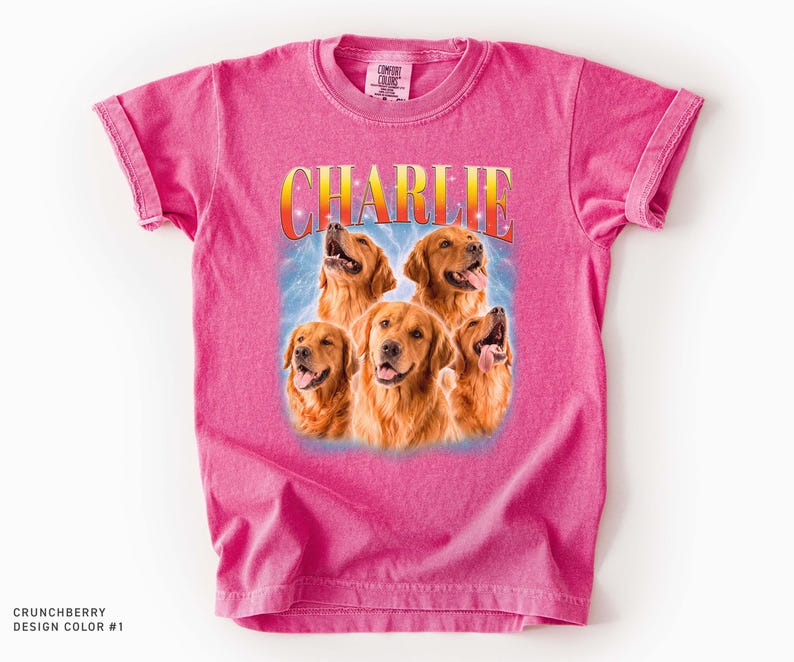 May include: A bright pink short-sleeve t-shirt featuring a graphic print of five golden retriever dogs. Above the dogs, the name CHARLIE is printed in a yellow and orange gradient font. The background of the graphic shows a blue light effect.