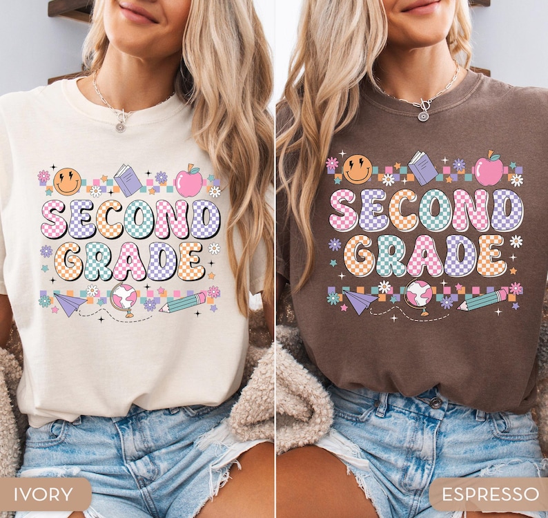 May include: Ivory and espresso-colored t-shirts with a colorful "SECOND GRADE" graphic. The design includes a smiley face, book, apple, globe, pencil, and floral accents. The shirts are paired with denim shorts.