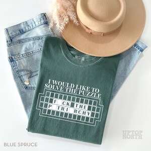 May include: A green t-shirt with the text "I would like to solve the puzzle" and a white scrabble board with the letters "FCK THE PTRI RCHY".