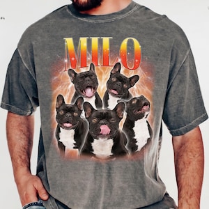 May include: A charcoal gray short-sleeve t-shirt featuring a graphic print of five French bulldogs. The text MILO appears in a yellow-to-red gradient font above the dogs, set against a fiery orange background. The shirt includes the text PEPPER DESIGN COLOR #4.