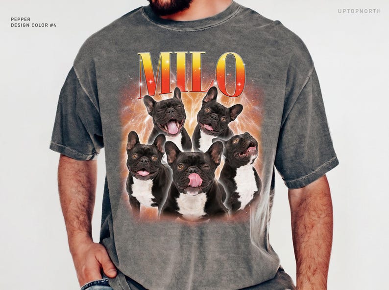 May include: A charcoal gray short-sleeve t-shirt featuring a graphic print of five French bulldogs. The text MILO appears in a yellow-to-red gradient font above the dogs, set against a fiery orange background. The shirt includes the text PEPPER DESIGN COLOR #4.