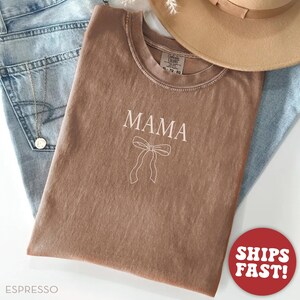 May include: A brown t-shirt with the word "MAMA" and a white bow printed on the front.
