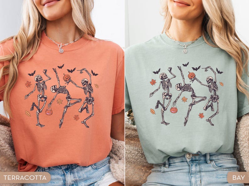 K&ouml;nnte beinhalten: Ein terrakottafarbenes T-Shirt und ein helles salbeigr&uuml;nes T-Shirt, beide mit einem Grafikdruck von drei tanzenden Skeletten, schwarzen Flederm&auml;usen und orangefarbenen Herbstbl&auml;ttern. Ein Skelett h&auml;lt einen K&uuml;rbis, ein anderes einen Eimer.