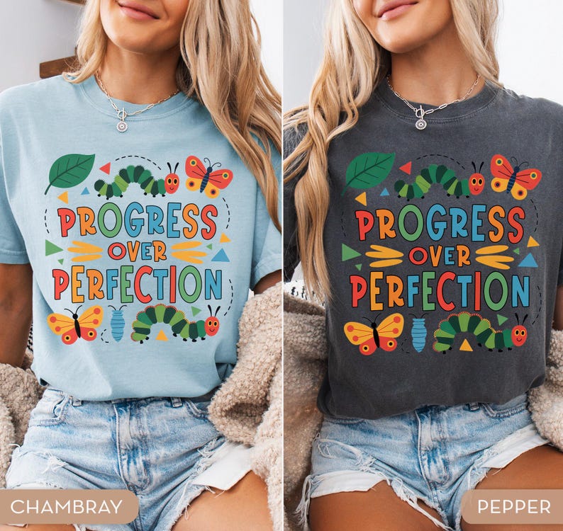 Op de afbeelding: Twee T-shirts, &eacute;&eacute;n lichtblauw en &eacute;&eacute;n donkergrijs, met de tekst "PROGRESS OVER PERFECTION" in kleurrijke letters. De shirts hebben illustraties van rupsen, vlinders en bladeren, wat een grillig ontwerp cre&euml;ert.