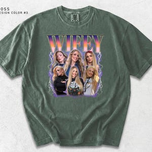 May include: Moss green t-shirt with a graphic of a group of women and the word "WIFEY" in a retro font. The shirt has a crew neck and short sleeves. The design is in shades of purple, orange, and white.