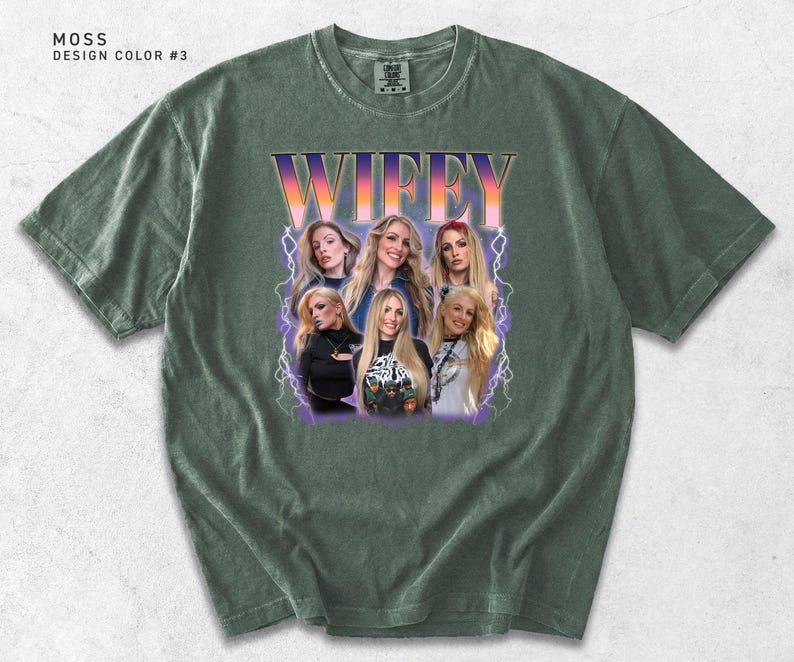 May include: Moss green t-shirt with a graphic of a group of women and the word "WIFEY" in a retro font. The shirt has a crew neck and short sleeves. The design is in shades of purple, orange, and white.