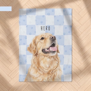 May include: A rectangular blanket featuring a light blue and white checkered pattern with small paw prints. The center displays a realistic illustration of a golden retriever with its mouth open and the text HERO printed above the dog.