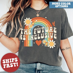 May include: Dark gray t-shirt with a retro rainbow design and the text "THE FUTURE IS INCLUSIVE." The design includes daisies, a butterfly, and a heart. The shirt has a vintage, worn look.
