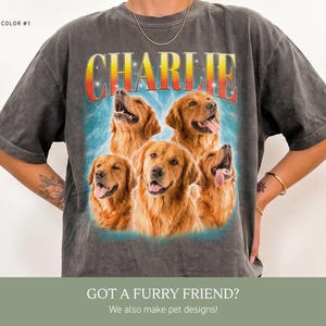 May include: A charcoal gray short-sleeve t-shirt featuring a graphic print of five golden retriever dogs. Above the dogs, the name CHARLIE is printed in a bold, red-to-yellow gradient font. The background of the graphic includes blue lightning.