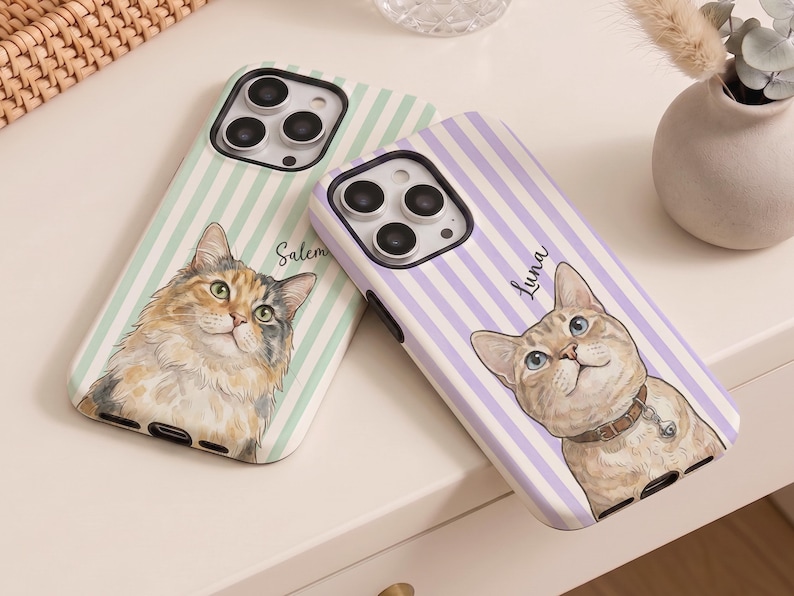 May include: Two phone cases featuring cat illustrations. One case has a green and white striped background with a cat illustration and the name "Salem". The other case has a purple and white striped background with a cat illustration and the name "Luna".