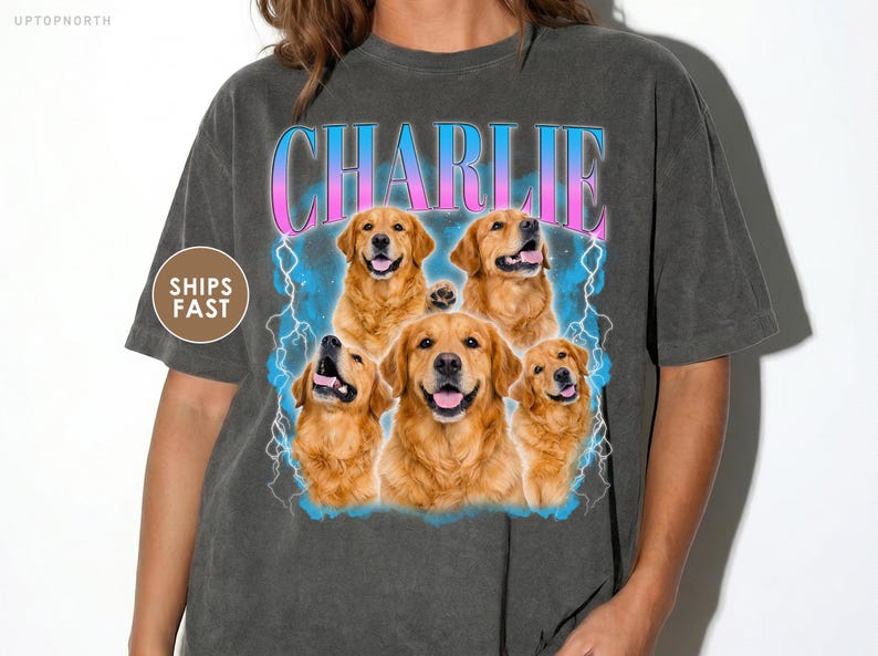 May include: A charcoal gray short-sleeve t-shirt featuring a graphic print of five golden retriever dogs. The text CHARLIE appears in a blue and pink gradient font above the dogs, surrounded by blue lightning bolt illustrations on a blue cloud background.