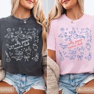 May include: Two t-shirts, one pepper-colored and one blossom-colored, each featuring a whimsical design of ducks and the text "silly goose mama club." The shirts are made of a soft material and are suitable for casual wear.
