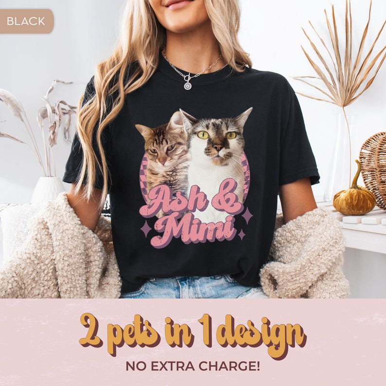 May include: Black t-shirt featuring a graphic of two cats, with the names "Ash & Mimi" in pink script. The design is set within a pink circle with purple star accents. The text "2 pets in 1 design" and "NO EXTRA CHARGE!" is below the graphic.